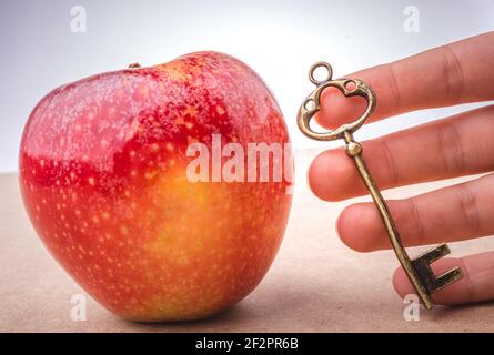 Hand mit einem Schlüssel neben einem roten Apfel Stockfoto