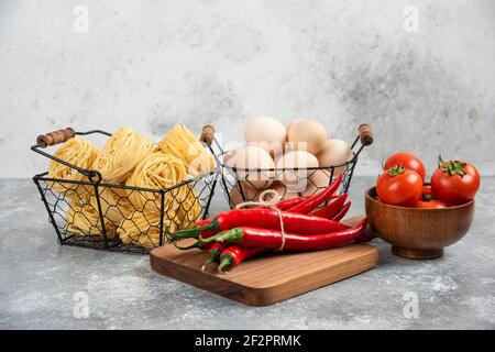 Korb mit rohen Nudeln, Tomaten, Chilischoten und Eiern auf Marmoroberfläche Stockfoto