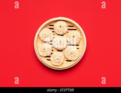 Ungekochte Schweinefleisch Baozi Knödel in Bambus-Dampfer, isoliert auf rotem Hintergrund. Rohes chinesisches Essen, flaches Lay. Kochen gedämpfte bao Buns, über Ansicht. Stockfoto