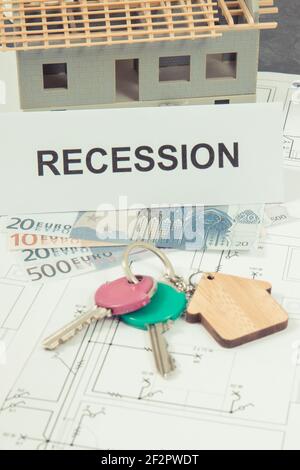 Schlüssel mit Home Form, Währungen Euro und Beschriftung Rezession auf elektrischen Bauzeichnungen. Konzept der Immobilienkrise. Kleines Haus unter Stockfoto