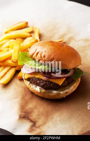 Leckere hausgemachte Burger mit knusprigen Pommes serviert. Rustikale Hamburger und Kartoffelchips Komposition mit Backpapier und Holztisch. Stockfoto