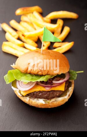 Leckere hausgemachte Burger mit knusprigen Pommes serviert. Rustikale Hamburger und Kartoffelchips Komposition mit Backpapier und Holztisch. Stockfoto