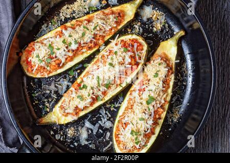 Zucchini Boote gefüllt mit Hackfleisch, gehackte Tomaten und Käse in einer schwarzen Backform auf einem Holztisch, italienische Küche Stockfoto