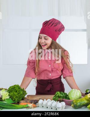 Happy teen Mädchen Kochen Gemüse. Kind trägt professionelle Koch Uniform. Stockfoto