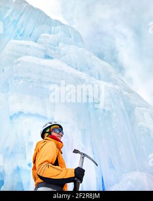 Frau Kletterin in oranger Jacke mit Eispickel in der Nähe gefroren Wasserfall in den Bergen Stockfoto