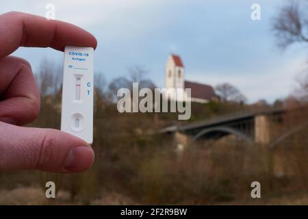 Kassette mit negativem covid-19-Testergebnis wird von Hand zwischen den Fingern gehalten. Stadtkirche steht auf dem Hügel hinter einer Brücke. sonnenaufgang. Stockfoto