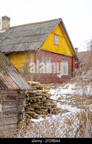 Pile und Wand aus geschnittenem Birkenholz und gestapelten Holzstämmen bereit für den Winter, auf dem Schnee in der Nähe eines litauischen typischen Holzhaus im Winter stehen Stockfoto