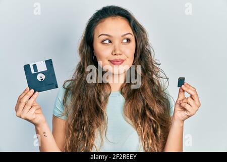 Junge hispanische Mädchen hält Diskette und sdxc-Karte lächelnd Blick zur Seite und starrte weg denken. Stockfoto