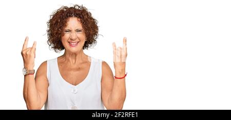 Schöne ältere Frau tragen lässige weiße Hemd schreien mit verrückten Ausdruck Rock-Symbol mit Händen nach oben. Musik-Star. Heavy-Konzept Stockfoto