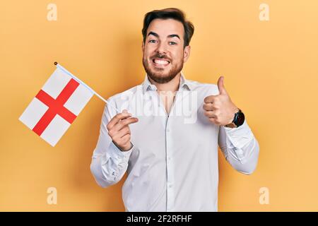 Schöner kaukasischer Mann mit Bart hält england Flagge lächelnd glücklich und positiv, Daumen nach oben tun ausgezeichnet und Zustimmung Zeichen Stockfoto