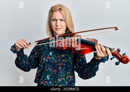 Junge blonde Frau spielt Geige ahnungslos und verwirrt Ausdruck. Zweifel Konzept. Stockfoto