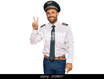 Schöner Mann mit Bart tragen Flugzeug Pilot Uniform zeigt und zeigt mit den Fingern Nummer zwei, während lächelnd zuversichtlich und glücklich. Stockfoto