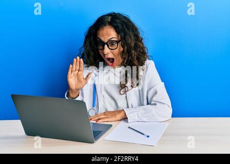 Schöne mittlere Alter Arzt Frau tun Video-Anruf winken zu Laptop Angst und schockiert mit Überraschung und erstaunt Ausdruck, Angst und aufgeregt Gesicht. Stockfoto