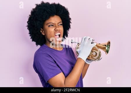 Junge afroamerikanische Frau spielt Trompete wütend und wütend schreien frustriert und wütend, schreien vor Wut. Wut und aggressive Konzept. Stockfoto