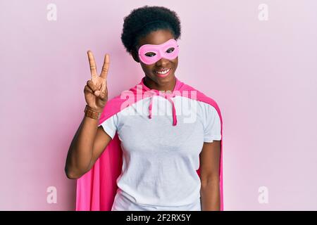 Junge afroamerikanische Mädchen trägt Superhelden Maske und Cape Kostüm zeigt und zeigt mit den Fingern Nummer zwei, während lächelnd zuversichtlich und glücklich. Stockfoto