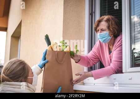 Frau, die Lebensmittel und Lebensmittel an ihre ältere Mutter liefert. Soziale Distanzierung durch Sperrung der Coronavirus-Pandemie Stockfoto