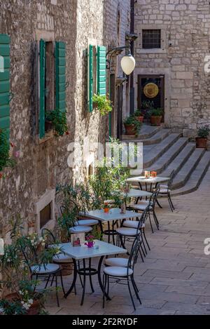 Restauranttische in einer engen Straße in der Altstadt von Sibenik, Kroatien Stockfoto