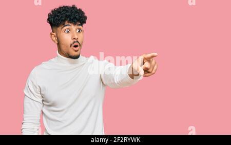 Junger arabischer Mann trägt lässigen Winter Pullover mit Finger überrascht voraus, offenen Mund erstaunt Ausdruck, etwas auf der Vorderseite Stockfoto