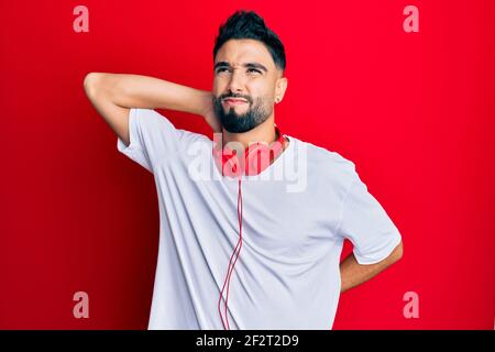 Junger Mann mit Bart Musik hören mit Kopfhörern leiden Nackenschmerzen Verletzung, berühren Hals mit der Hand, Muskelschmerzen Stockfoto