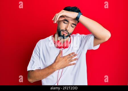 Junger Mann mit Bart, der Musik hört, mit Kopfhörern, die die Stirn berühren, wegen Krankheit und Fieber, Grippe und Erkältung, Viruskrankheit Stockfoto