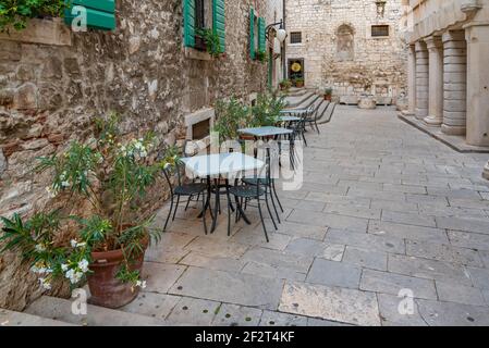 Restauranttische in einer engen Straße in der Altstadt von Sibenik, Kroatien Stockfoto