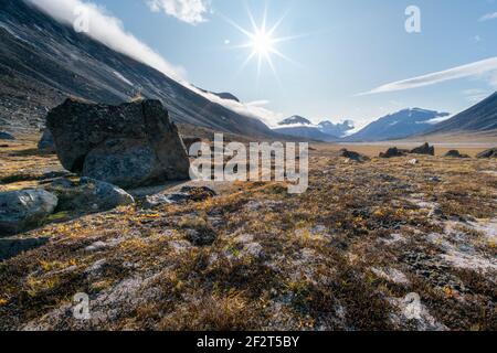 Sonnenstern scheint am Himmel über dem abgelegenen, wilden arktischen Tal des Akshayuk Pass, Baffin Island an einem sonnigen Sommertag. Ikonische Berge in der Ferne Stockfoto