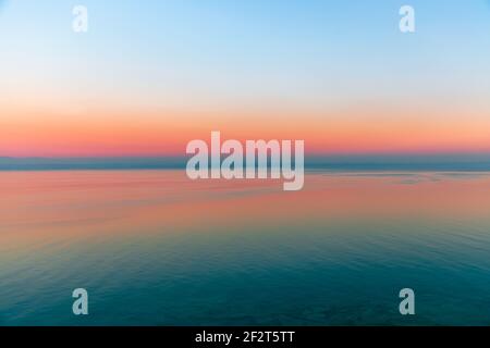 Schöner mehrfarbiger Sonnenuntergang spiegelt sich in den Gewässern des Gardasees, Italien. Skyline. Sichtbare Küste im Abendnebel. Winterzeit. Blick vom Si Stockfoto