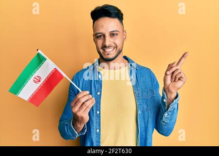 Junger arabischer Mann hält iran Flagge lächelnd glücklich zeigt mit Hand und Finger zur Seite Stockfoto