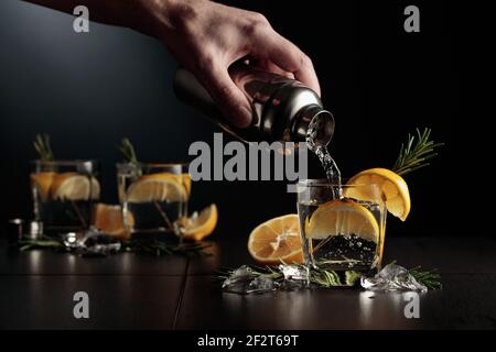 Cocktail Gin-Tonic mit Zitrone und Rosmarin. Der Barkeeper gießt einen Cocktail aus einem Shaker in ein Glas. Stockfoto