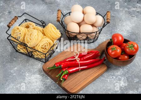 Korb mit rohen Nudeln, Tomaten, Chilischoten und Eiern auf Marmoroberfläche Stockfoto