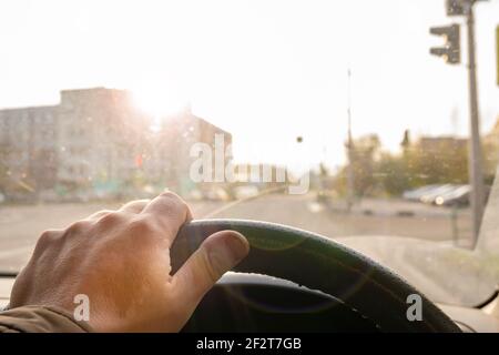 Die Hand des Fahrers am Lenkrad eines Autos Das wird durch helles Sonnenlicht in der Windschutzscheibe geblendet, während Fahren auf der Straße Stockfoto