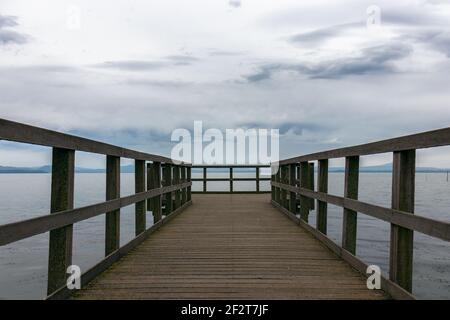 Schöne Aussicht auf den Trasimenischen See vom Pier aus. Der Himmel ist bedeckt und ruhiges Wasser, keine Menschen. Nostalgische Stimmung. Umbrien, Italien Stockfoto