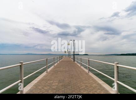 Schöne Aussicht auf den Trasimenischen See vom Pier aus. Der Himmel ist bedeckt und ruhiges Wasser, keine Menschen. Nostalgische Stimmung. Umbrien, Italien Stockfoto