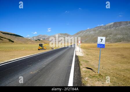 Leere Asphaltstraße über den malerischen Pian Grande in Castelluccio di Norcia, Umbrien, Italien. Straßenarbeiten entlang der Straße Stockfoto