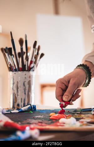 Künstler mischen Acrylfarben auf Palette für Malerei. Frau, die in ihrem Kunststudio arbeitet. Weibliche Hand mit Farbtube Stockfoto
