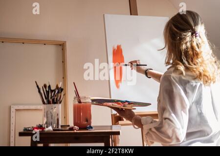 Frau Künstlerin Malerei in ihrem Kunststudio. Rote Acrylfarbe auf Leinwand. Kreative Hobbys und Freizeitaktivitäten Stockfoto