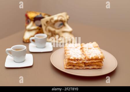 Typische italienische Karnevalsfritter (Chiacchiere di Carnevale) mit Puderpulver bestäubt. Zusammensetzung mit zwei Tassen Kaffee und im Hintergrund sind Venet Stockfoto