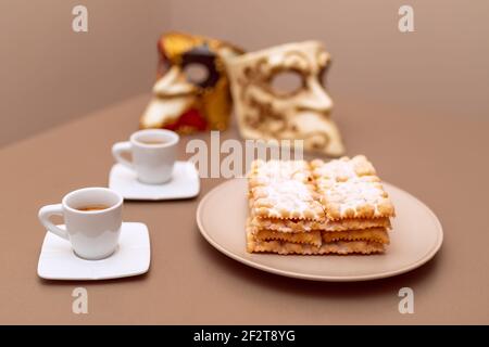 Typische italienische Karnevalsfritter (Chiacchiere di Carnevale) mit Puderpulver bestäubt. Zusammensetzung mit zwei Tassen Kaffee und im Hintergrund sind Venet Stockfoto