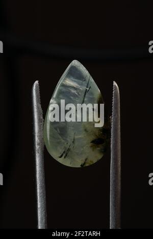 Naturstein aus Phnit in Pinzette auf schwarzem Hintergrund Stockfoto