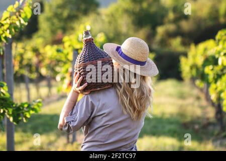 Frau mit Demijohn im Weinberg. Tradition Erntefest. Junge Frau hält die Ballonflasche mit Wein Stockfoto