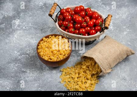 Rustikale Körbe von Pasta mit Kirschtomaten auf Marmor Hintergrund Stockfoto