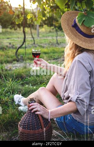 Frau, die Rotwein im Weinberg verkostet. Junger Bauer trinkt hausgemachten Wein im Freien. Freude am Leben Stockfoto