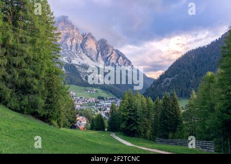 Ein Weg, der durch eine Almwiese zum Dorf führt Von Corvara am Fuße der Dolomiten in Italien Stockfoto