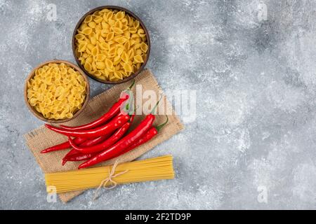 Holzschüsseln roher Pasta mit roten Chilischoten auf Marmorhintergrund Stockfoto