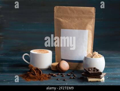 tasse Kaffee, Kaffeebohnen, Zucker, Bastelpapierbeutel, Makronen und Schokolade auf Holzhintergrund Stockfoto