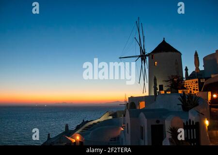Eine alte Windmühle im Dorf Oia auf der Insel Santorini, Griechenland bei Sonnenuntergang. Im Hintergrund der blaue Himmel und das Mittelmeer. Stockfoto