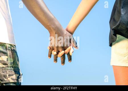 Multirassisches Paar, das Hand in Hand gegen einen blauen Himmel geht - Konzept der multiethnischen Liebe über soziale Barrieren Stockfoto