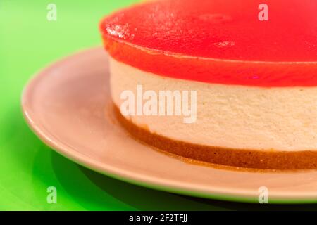 Selbstgemachter Käsekuchen mit Wassermelonengelee auf der Oberseite, auf einem hellen kontrastierenden grünen Hintergrund (Makrofoto, selektiver Fokus) Stockfoto