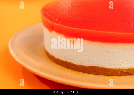 Selbstgemachter Käsekuchen mit Wassermelonengelee auf der Oberseite, auf einem hellen orangenen Hintergrund (Makrofoto, selektiver Fokus) Stockfoto