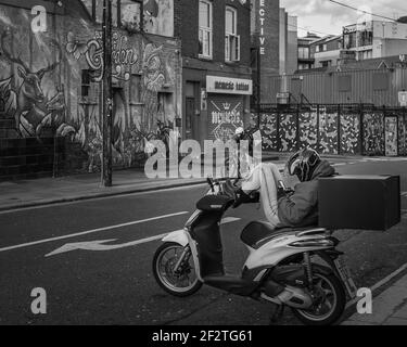 Ein monochromes Bild eines Lieferfahrers, der eine Pause einnimmt, während er auf seinen nächsten Einsatz wartet. Stockfoto